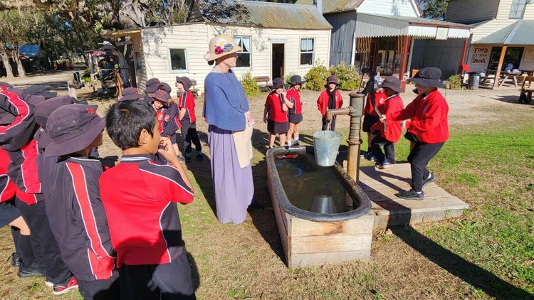 Students on an colonial excursion looking at an old hand water pump